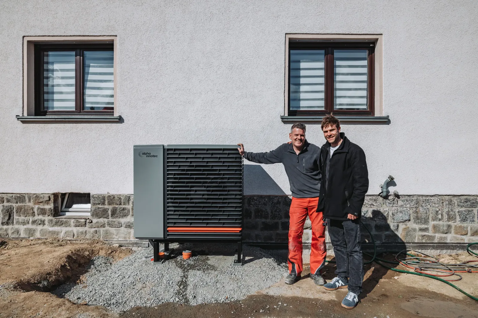 Zwei Vendix-Monteure stehen neben einer frisch installierten Wärmepumpe vor einem Haus.